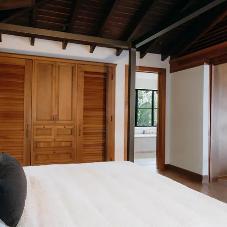 Royal Isabela Hotel Exterior photo This is a photograph of a bright and modern bedroom with a rustic, exposed-beam architectural style.

**Key features in the image include:**

*   **The Bed:** In the foreground, there is a large, inviting bed covered with crisp white linens. A dark g